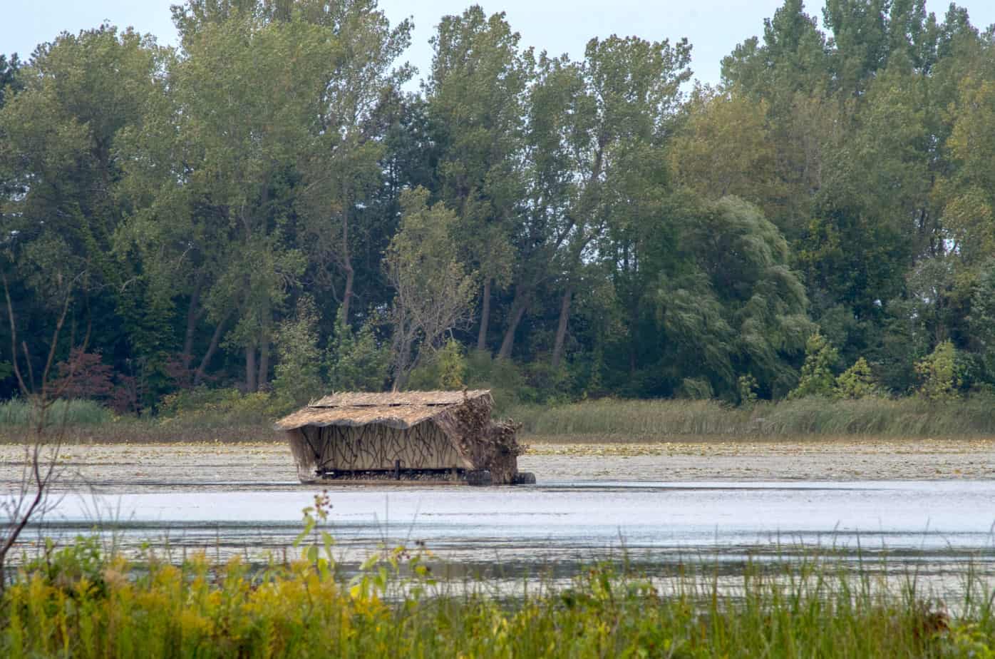 A small building sitting on a little pond in Michigan USA, is a duck blind, used to hide hunters who like to shoot the traveling ducks and geese