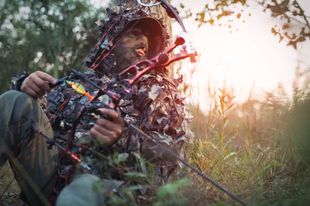bow hunter hunting from the ground and using a tree as cover.