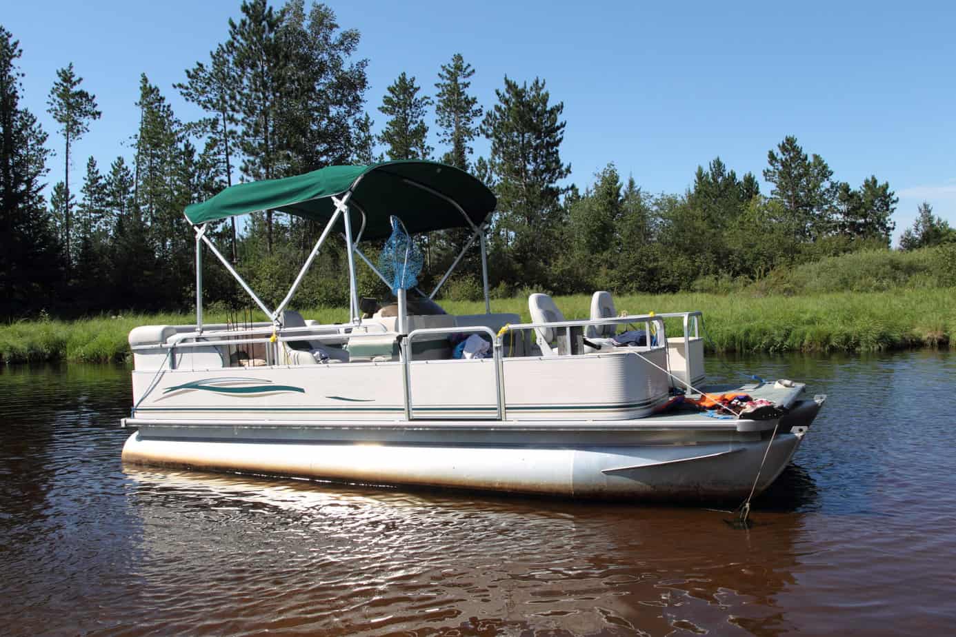 A big pontoon boat anchored in the river with fishing poles and the canopy up.