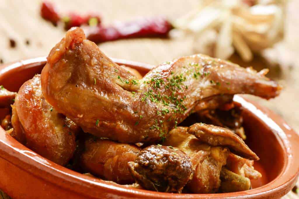 closeup of an earthenware with conejo al ajillo, a typical spanish recipe of rabbit with garlic an parsley, on a rustic wooden table