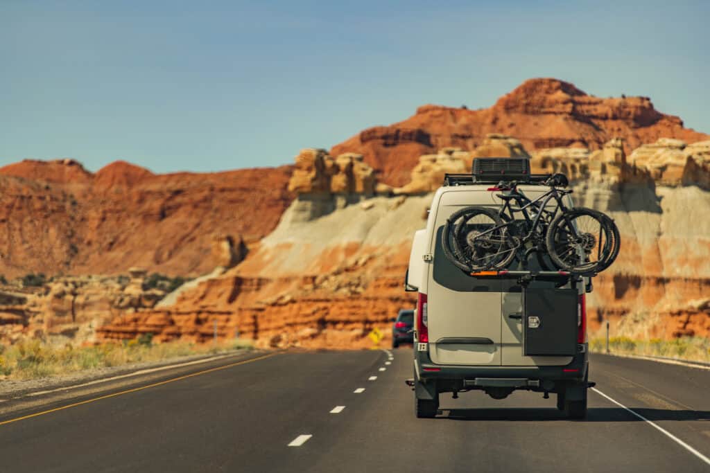 Modern Class B Camper Van Motorhome on Scenic Route with Back Vehicle Bikes Rack. Outdoors and Recreation Theme.