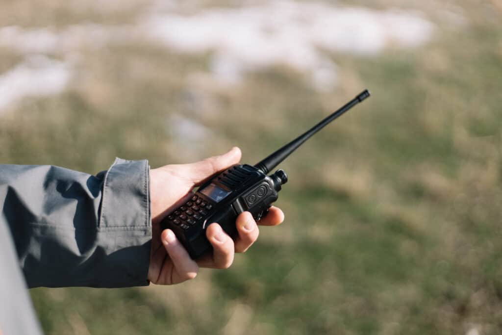 Close-up of a mans hand holding GMRS radio. Mountain walkie-talkie in man's hand against blurred grass background.